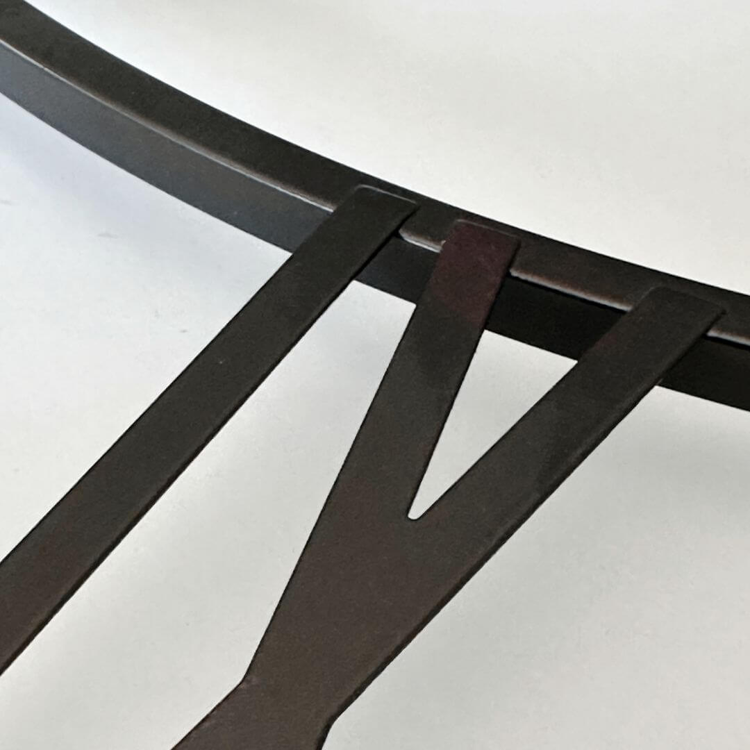 Close-up view of black Roman numerals with copper undertone on metal wall clock