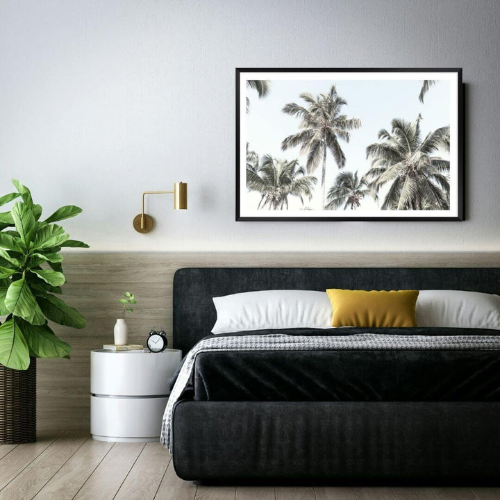 A wall art photo print of coastal palm trees and blue sky with a black frame for the wall in your bedroom