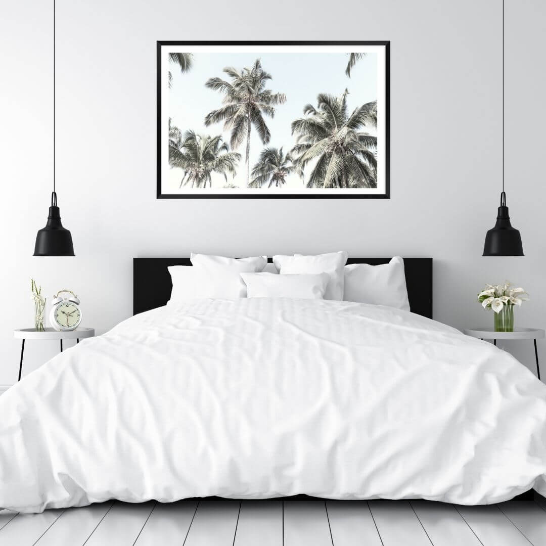 A wall art photo print of coastal palm trees and blue sky with a frame in black to style a wall in bedroom