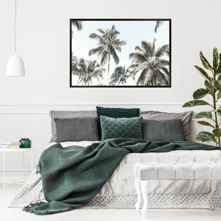 A wall art photo print of coastal palm trees and blue sky with a black frame, no border on bedoom wall