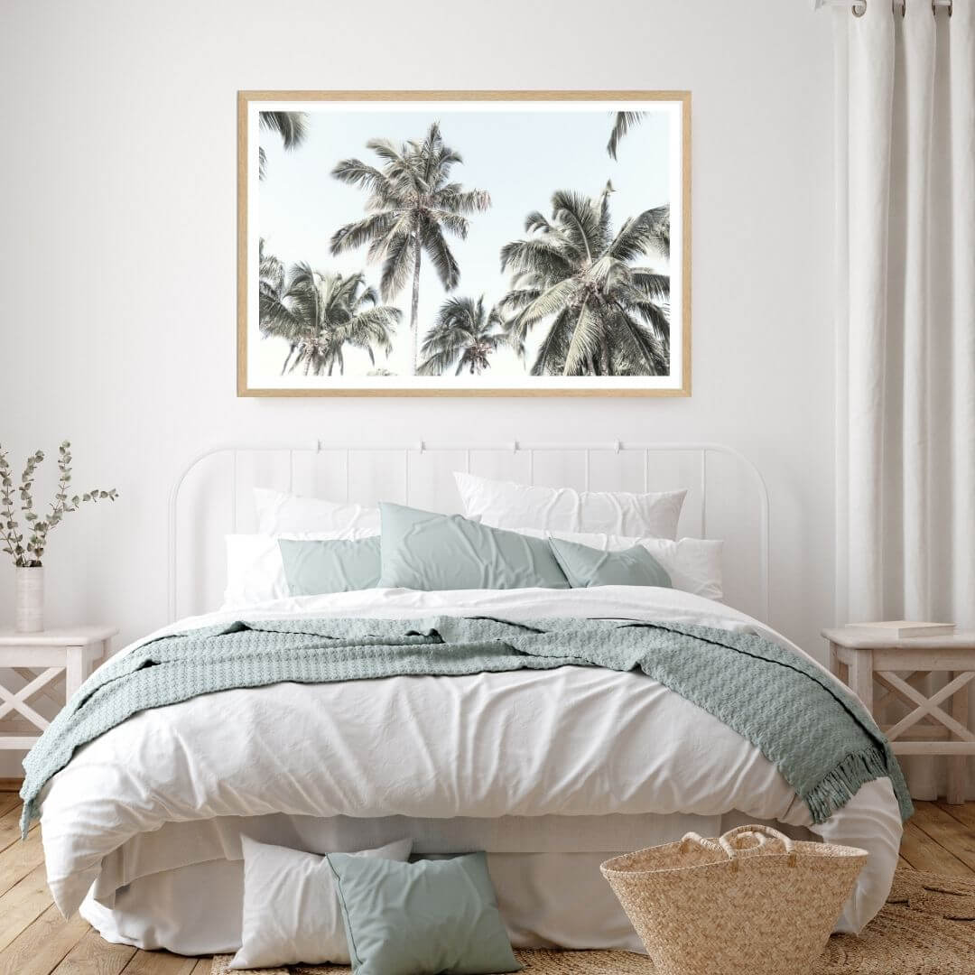 A wall art photo print of coastal palm trees and blue sky with a timber frame to decorate your bedroom empty walls