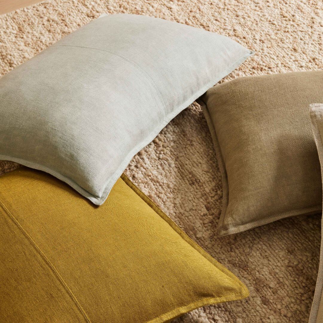 Como 50cm square linen cushion alongside rectangle linen cushions on a natural rug