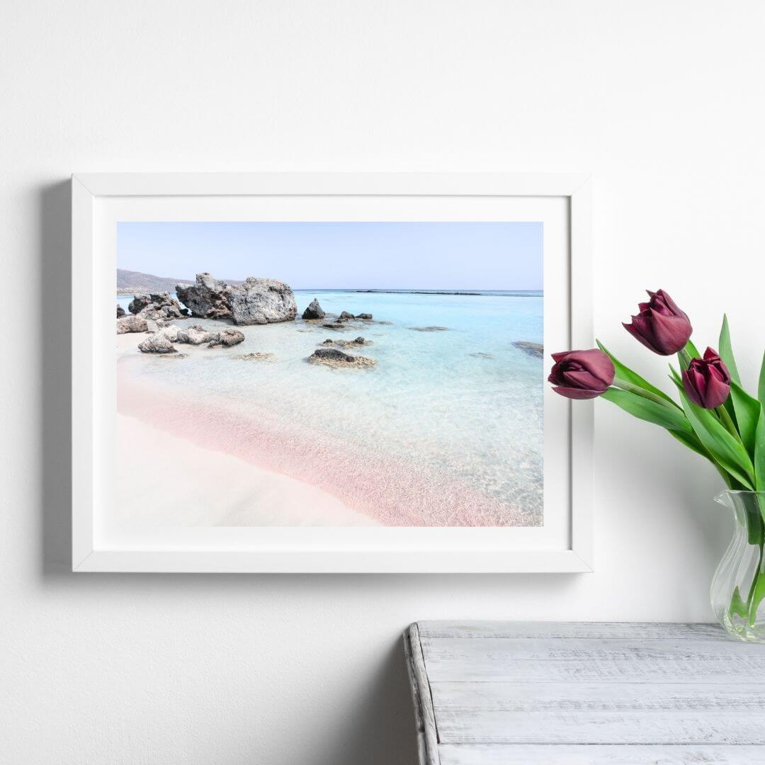 A coastal wall art photo print of a pink beach in Greece with a white frame or unframed to style shelves and empty walls