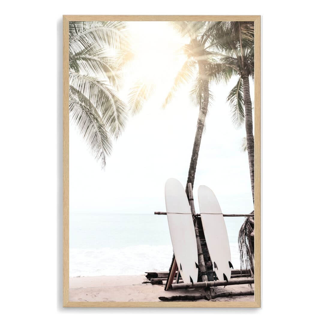A photo wall art print of two white surf boards under the palm trees on a surfer beach in Hawaii in a timber frame.