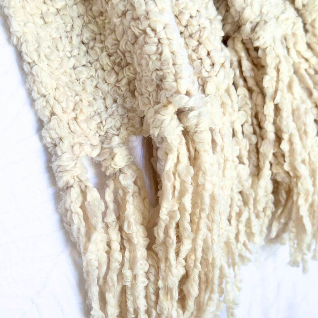 A cream tasseled Jade Throw with a boucle design, measuring 130cm x 160cm to style your bed or sofa.