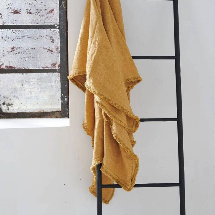 A tumeric yellow decorative Luca linen throw styled on a ladder at Beautiful Home Decor