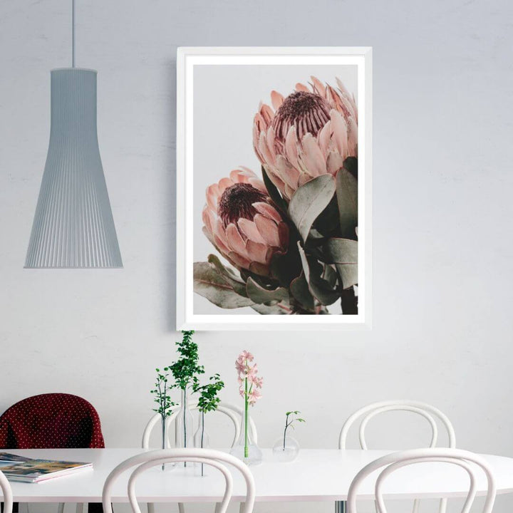 The wall art photo print of a peach protea floral b with a white frame, white border on dining room wall