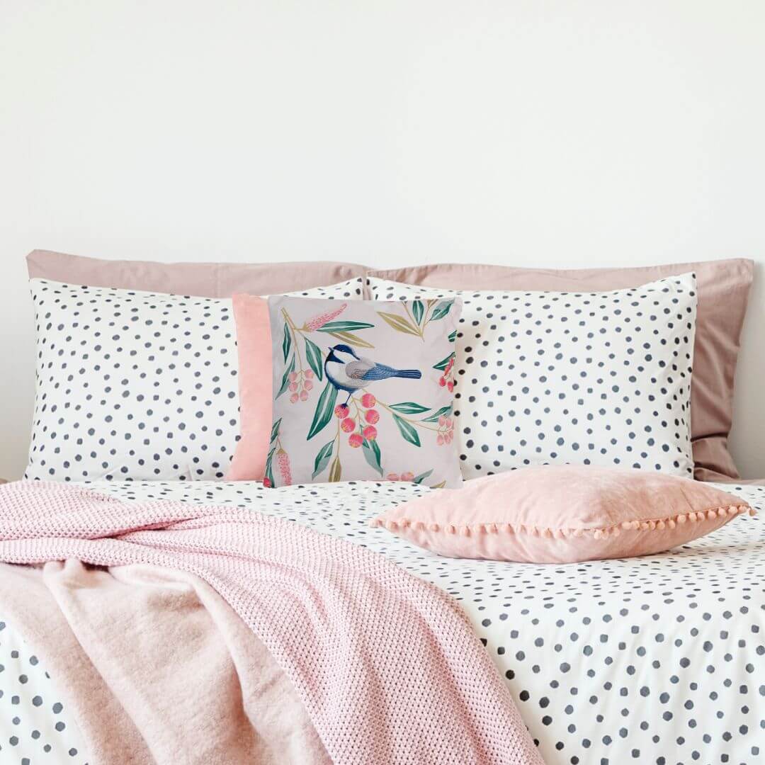 A pretty bird cushion styled on a pink and white bed in a girls bedroom
