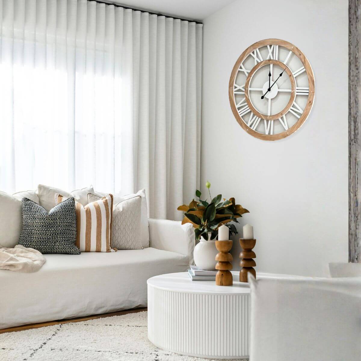 Living room with a white sofa, decorative pillows, a wooden coffee table, and a large coastal hamptons wall clock