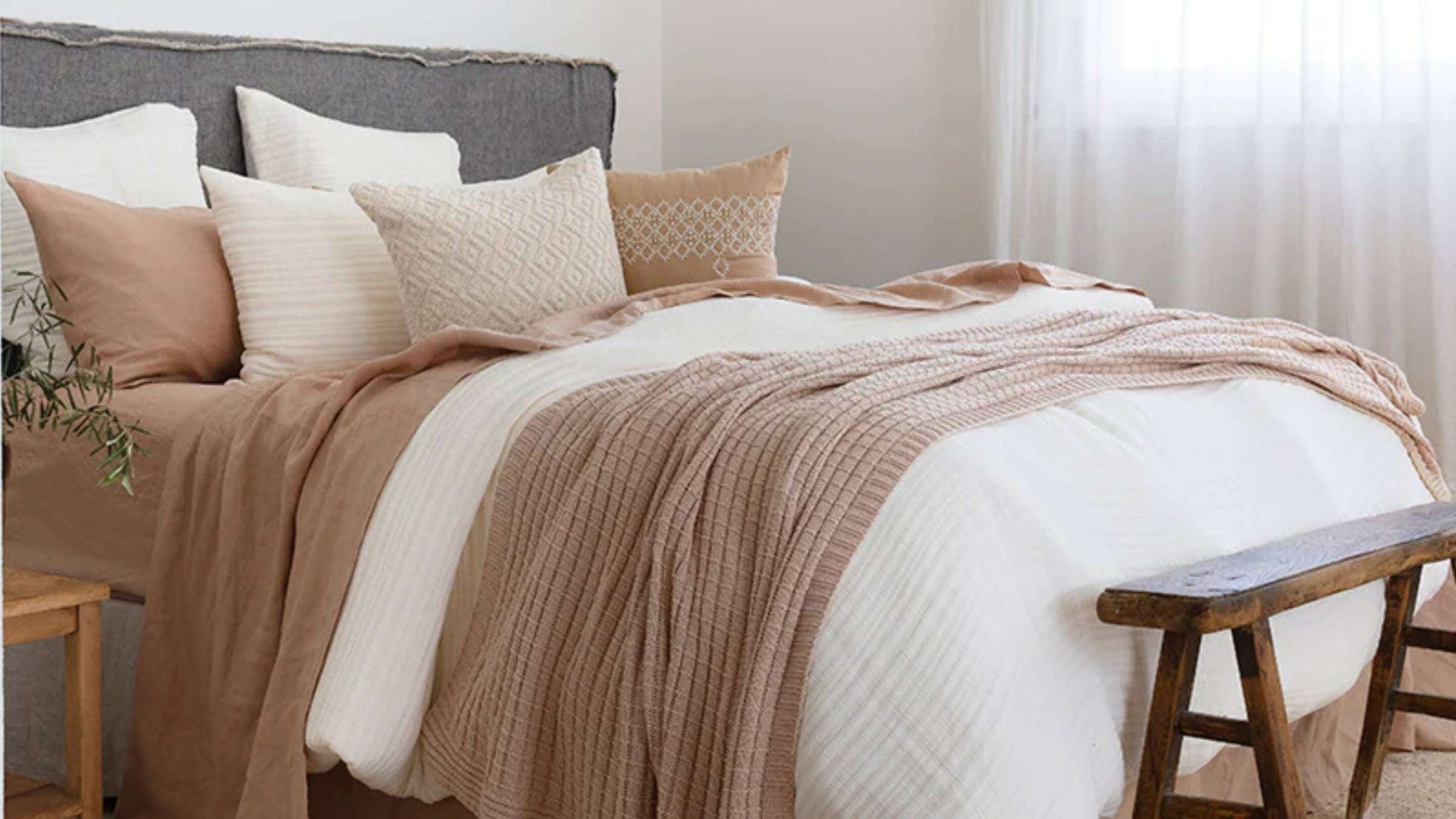 A beautifully styled bed with cushions and throws in neutral tones from Beautiful Home Decor