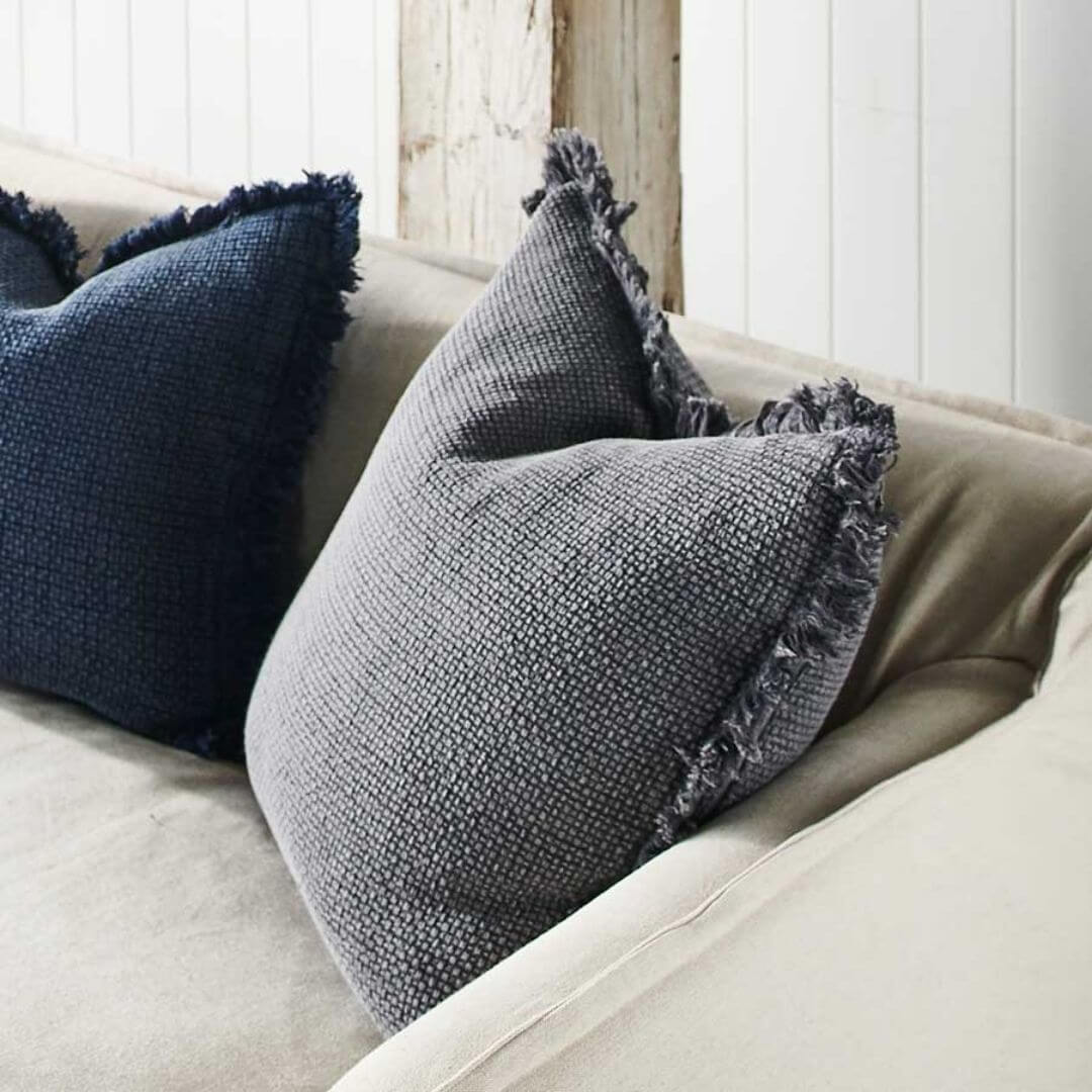 A slate grey Square 60cm Chelsea Fringe Cotton Cushion next to a matching Navy blue 50cm cushion. 
