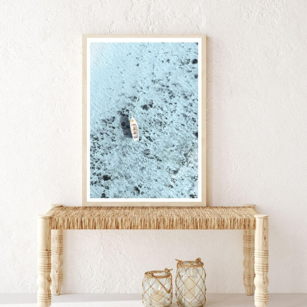 Coastal wall art print of a white boat on blue ocean with timber frame, styled in a hallway – Beautiful Home Decor.