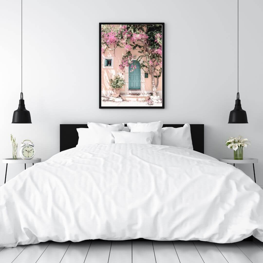 A Greek Pink Villa with Green Door Wall Art Photo Print framed in black above the bed by Beautiful Home Decor