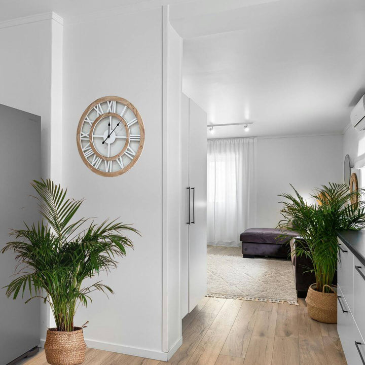 Modern interior with a large coastal hamptons wall clock on a white wall, plants, and a hallway leading to a living room.