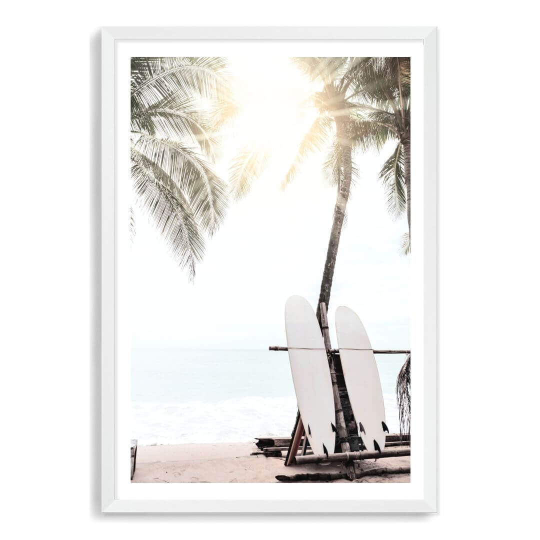 A wall art print of two white surf boards under the palm trees on a surfer beach in Hawaii in a white frame with a white border