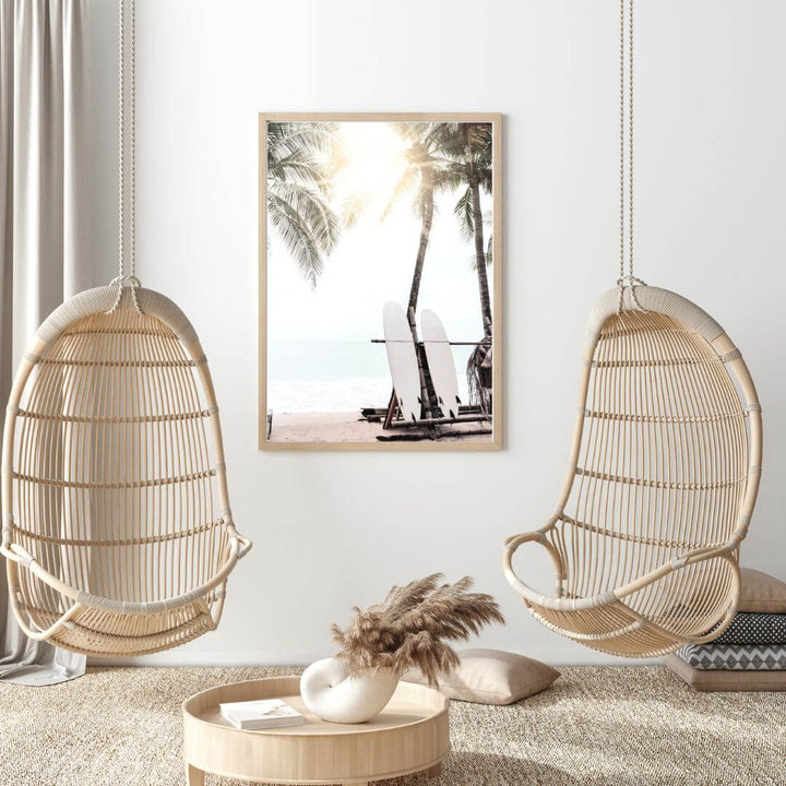 A relaxing coastal art print of two white surf boards under palm trees on a beach in Hawaii with the sun setting in the background. 