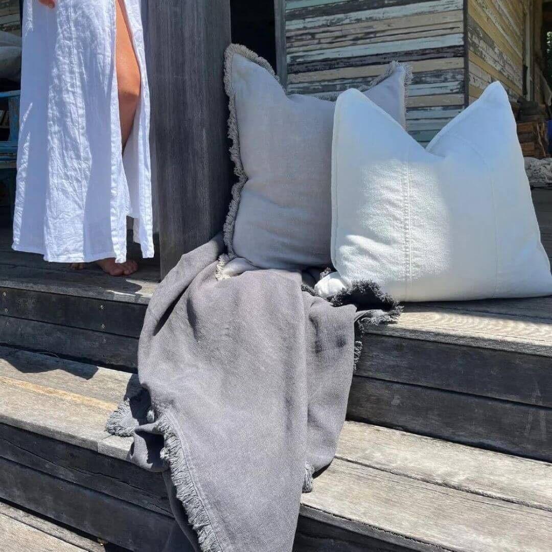 A slate grey Luca Boho Fringe Linen Throw measuring 150cm x 200 cm alongside matching cushions.