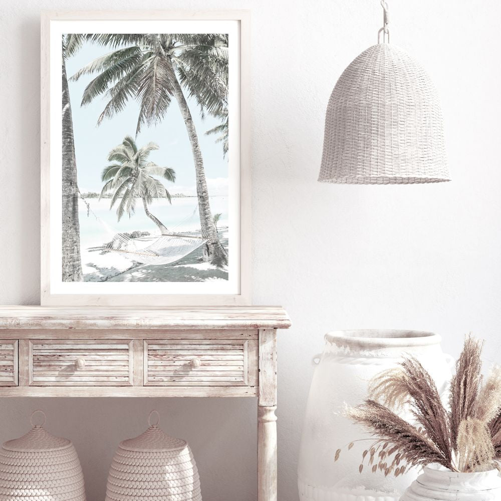 A photographic artwork of a hammock between two palm trees on a tropical beach, available in canvas or print, framed or unframed.