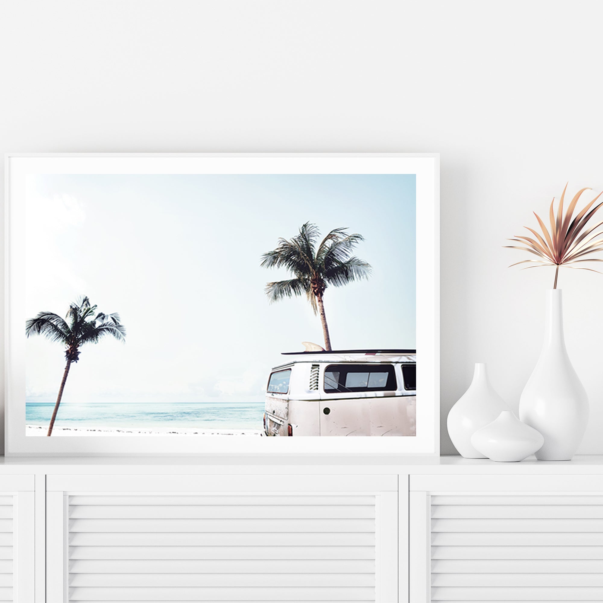 An artwork featuring an iconic blue Kombi van at the beach with palm trees, available in framed or unframed prints.