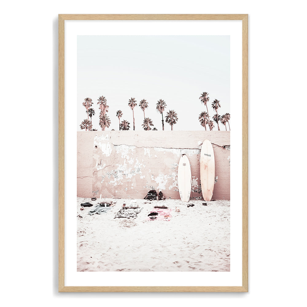 This coastal artwork featuring surf boards on the beach with palm trees and a wall is available in framed or unframed print.