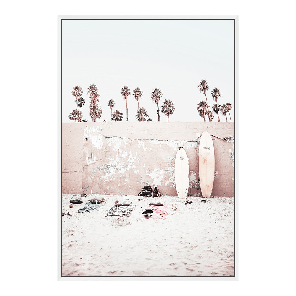 Available unframed or framed, this coastal artwork features surf boards on the beach with palm trees and a wall.