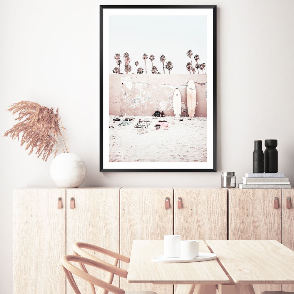 Available framed or unframed, this coastal wall art print features surf boards on the beach with palm trees and a wall.