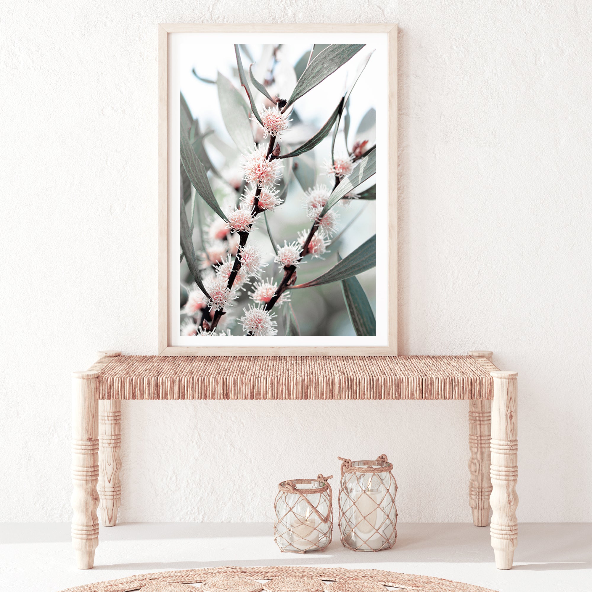 A framed or unframed Australian artwork of eucalytpus pink wild flowers and green leaves with branches in the background.
