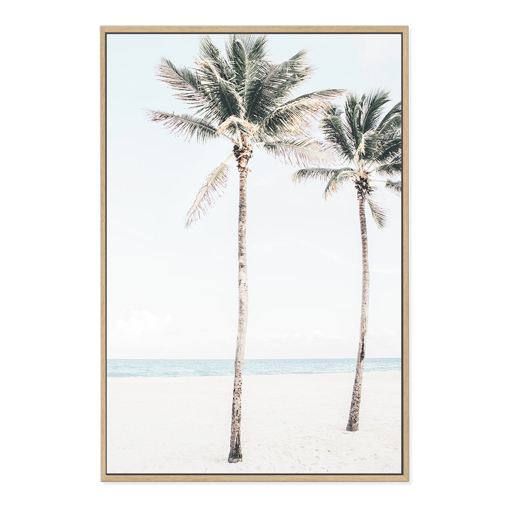 A Hamptons artwork of two palm trees, blue skies and the beach, available unframed or timber, black or white frames.