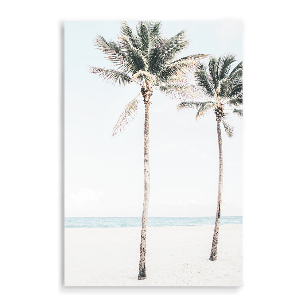 A stretched canvas coastal artwork of two palm trees, blue skies and the beach, available framed or unframed.