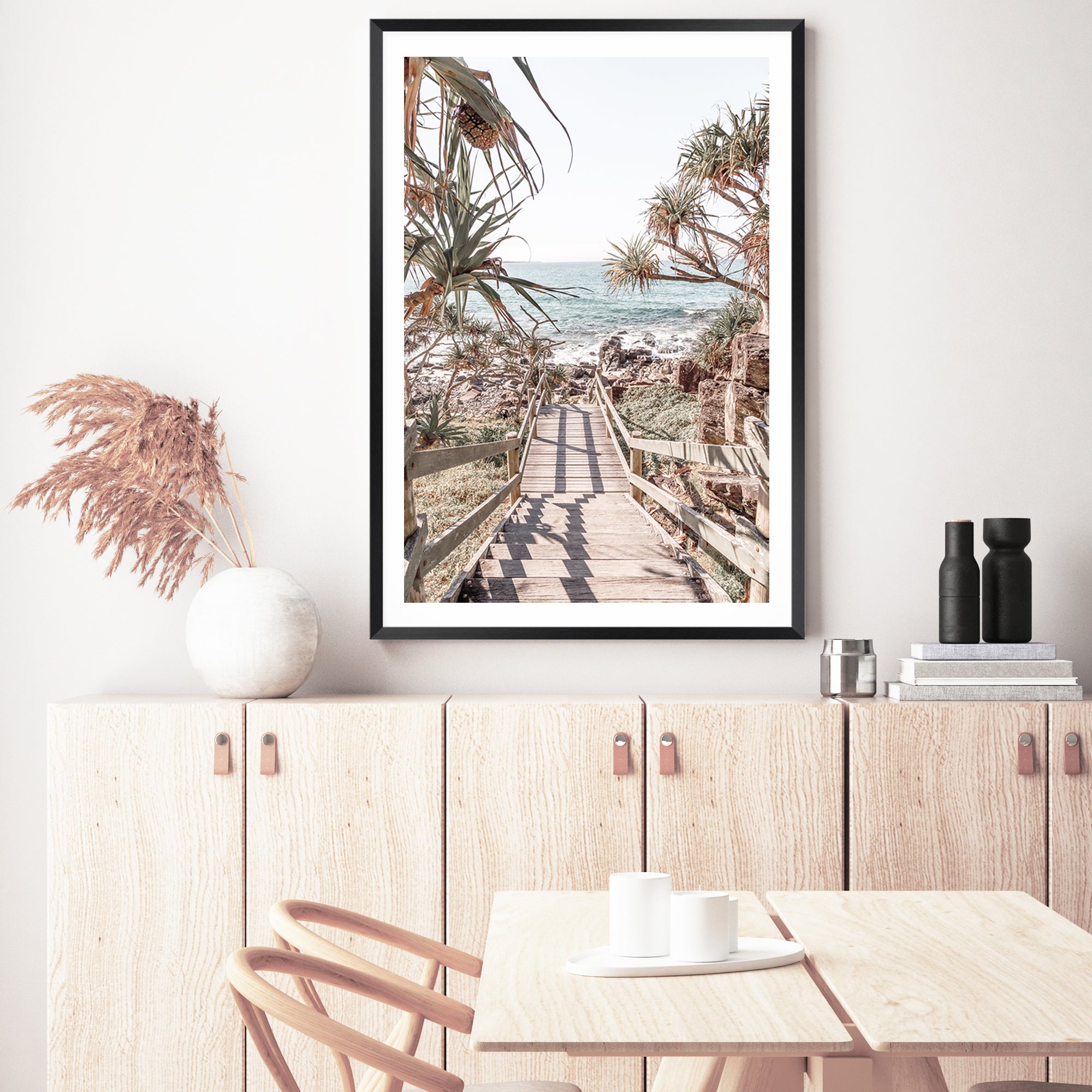 A coastal wall art of stairs leading onto a beach with beautiful blues of the sea and trees, available in print and canvas.